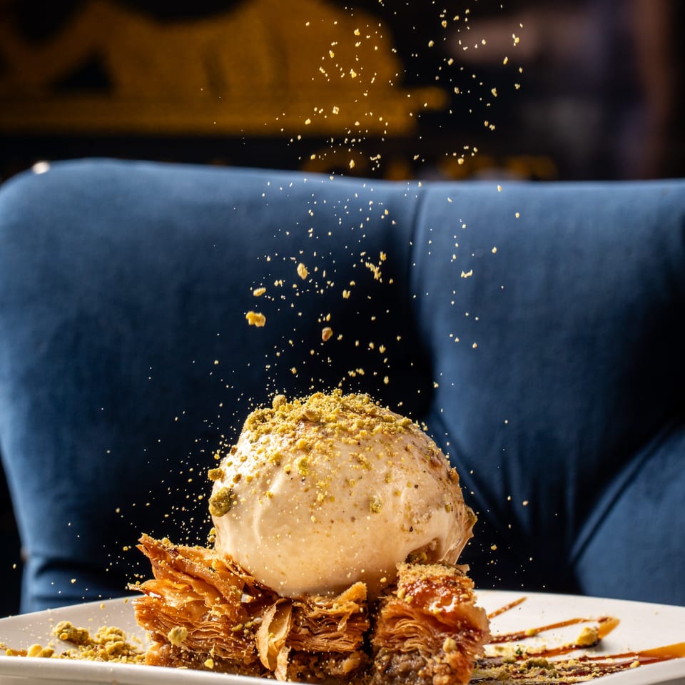 Baklava dessert with a scoop of ice cream and pistachio crumbles falling onto it.