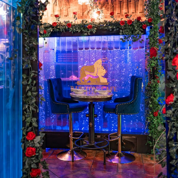 Babylon Cafe's intimate seating area with two blue velvet chairs, a small table, and a glowing blue waterfall.