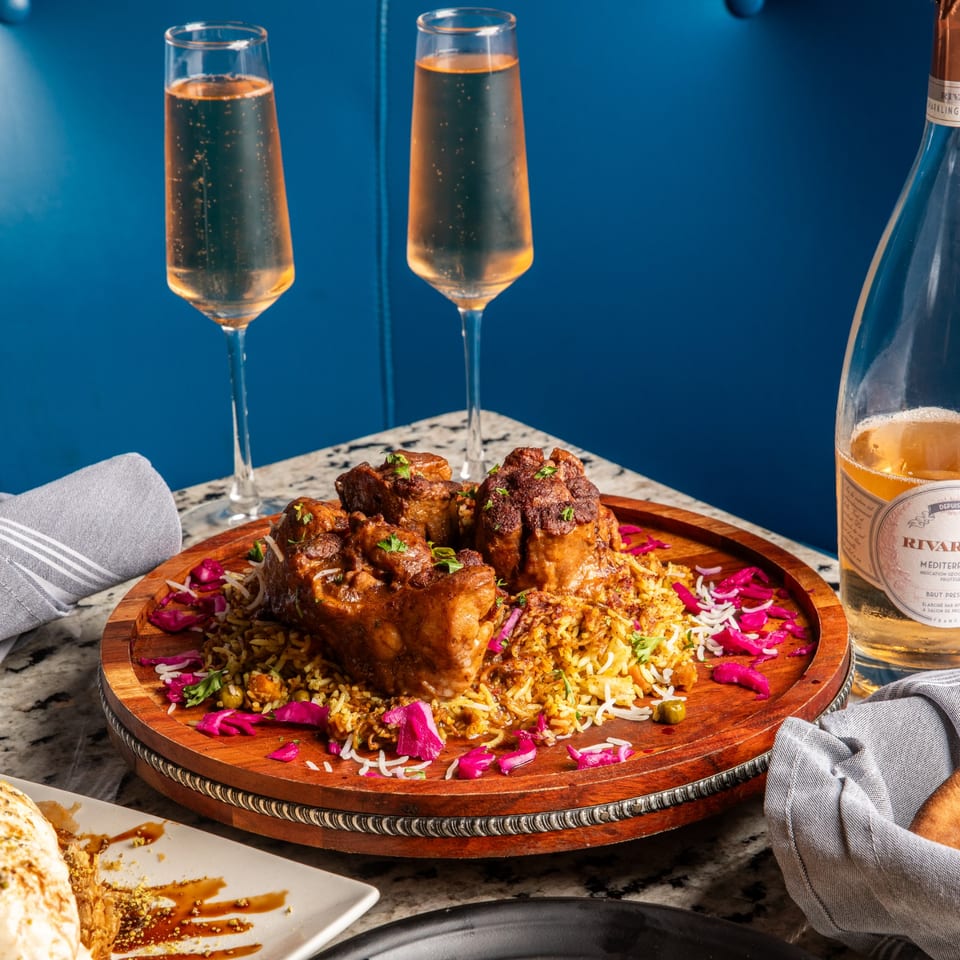 Middle-eastern lamb shanks on rice with pickled cabbage, two champagne flutes, and a wine bottle.