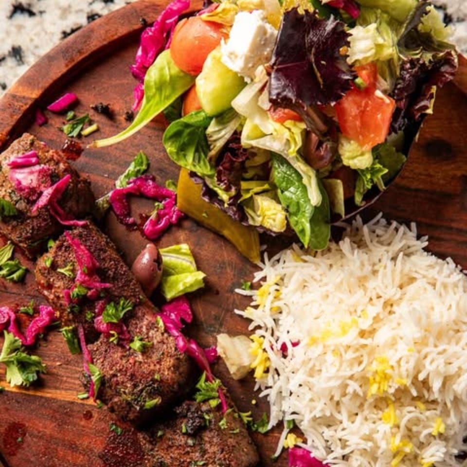 Middle-Eastern dish with grilled meat, pickled red onions, rice, and a fresh salad with feta.