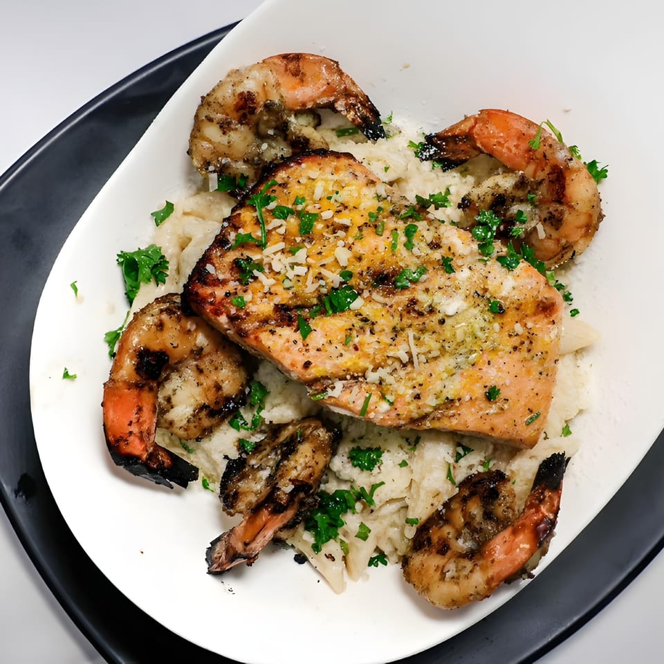 Grilled salmon and shrimp with rice, garnished with parsley and cheese, served on a white plate.