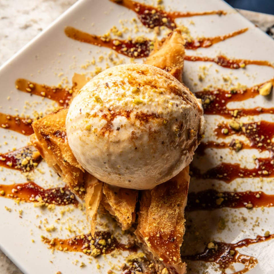 Baklava pieces topped with a scoop of ice cream, drizzled with syrup and sprinkled with nuts.