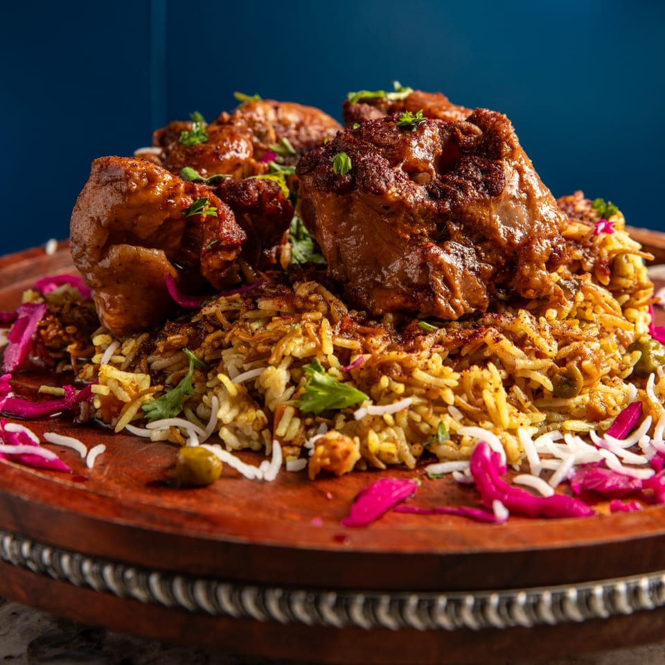 Middle-Eastern chicken and rice dish, garnished with pickled red cabbage and herbs on a wooden plate.