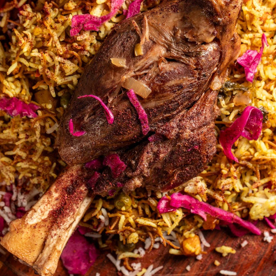Close-up of a lamb shank on a bed of seasoned rice with pickled red cabbage at Babylon Cafe.