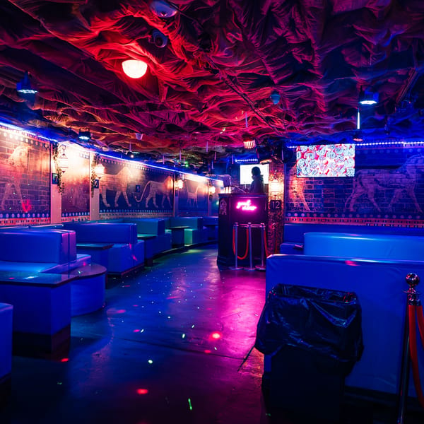 Babylon Cafe's vibrant interior with blue booths, Middle Eastern wall art, and a DJ booth under neon lights.