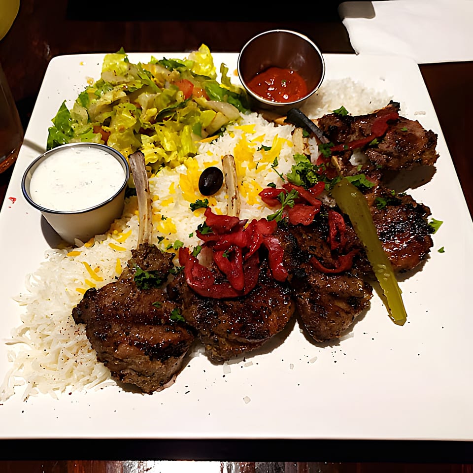 Grilled lamb chops with rice, salad, and sauces, a classic Middle Eastern dish from Babylon Cafe.