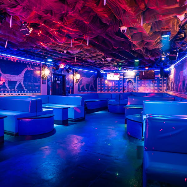 Babylon Cafe's interior with blue booths, Middle Eastern-inspired murals, and red and blue lighting.