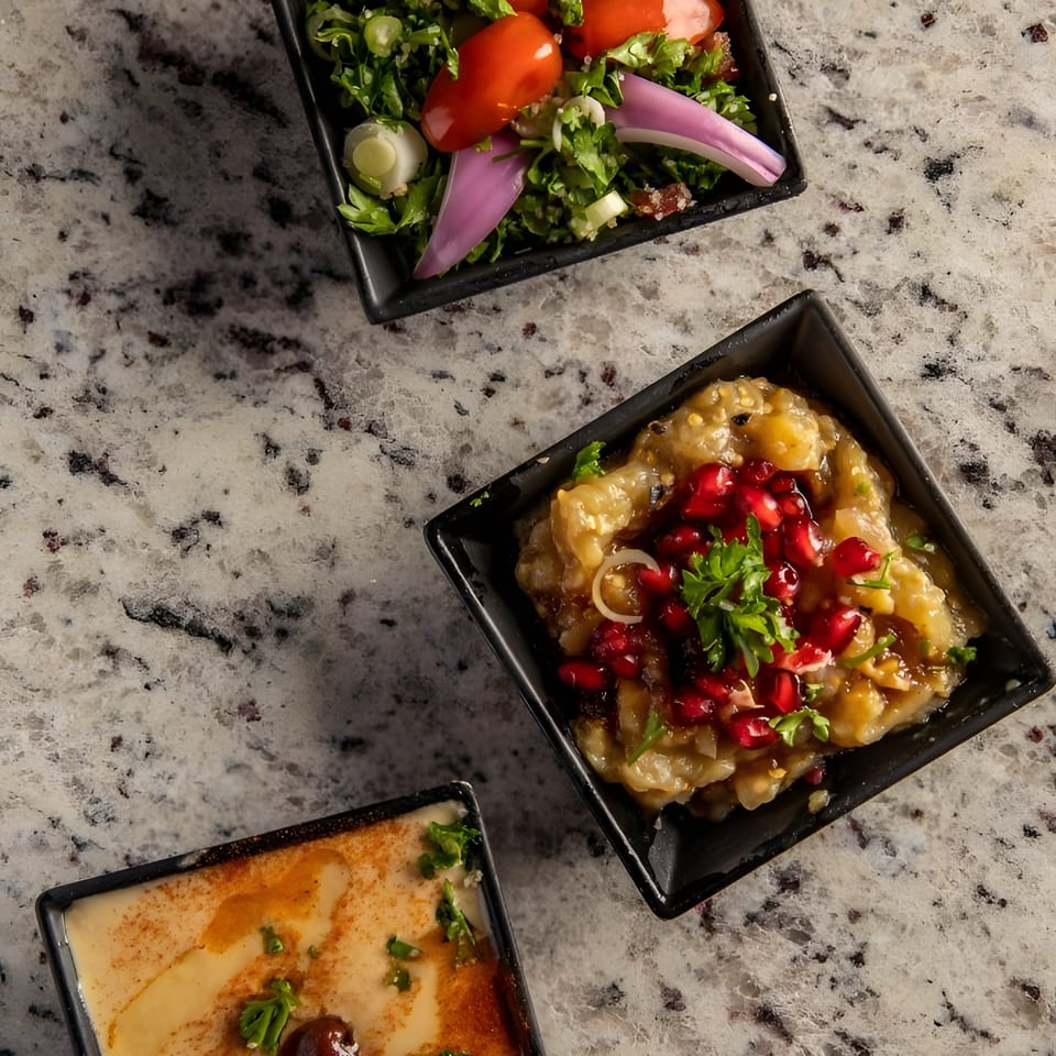 Three square bowls of Middle Eastern appetizers, including tabbouleh, baba ghanoush, and hummus.