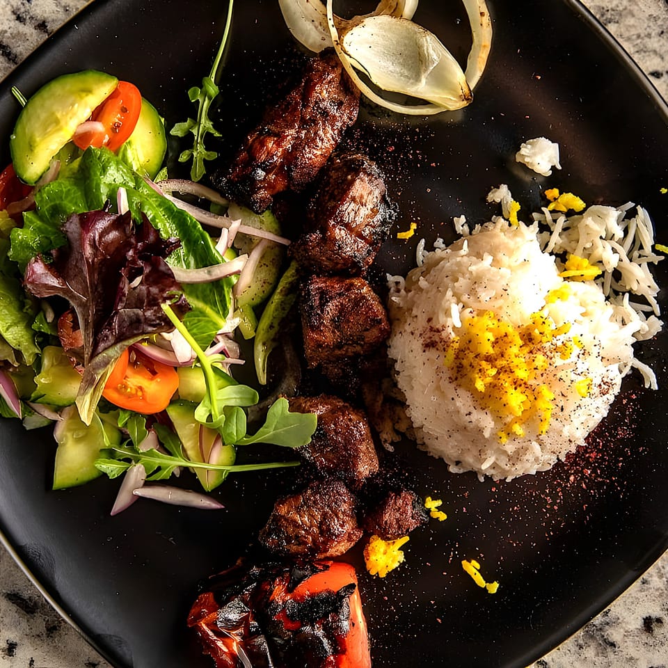 Middle-Eastern beef shish kebab with rice, grilled vegetables, and a fresh salad on a black plate.